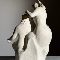 Alt text: Stylized, white sculpture of two women, one standing and one seated