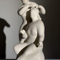 Alt text: Stylized, white sculpture of two women, one standing and one seated