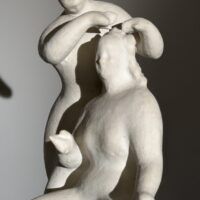 Alt text: Stylized, white sculpture of two women, one standing and one seated
