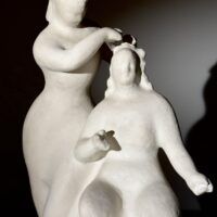 Alt text: Stylized, white sculpture of two women, one standing and one seated