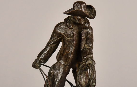 Alt text: Bronze sculpture of a standing cowboy with lasso, angled view