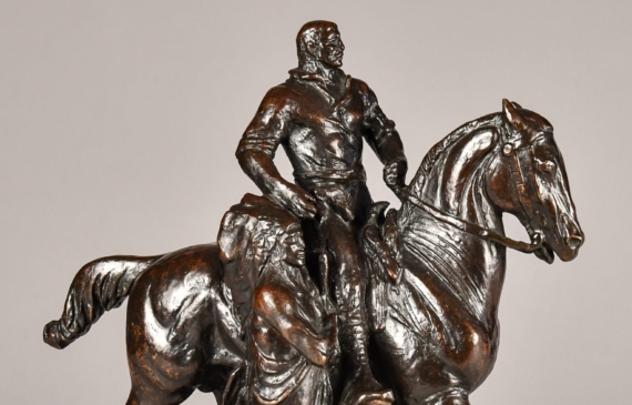 Alt text: Bronze sculpture of Teddy Roosevelt riding a horse flanked by two Native American men on the ground, side view