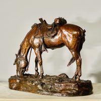 Alt text: Bronze sculpture of a saddled horse bending down to graze, angled view