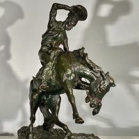 Alt text: Bronze sculpture of a cowboy riding on a bucking bronco, angled view