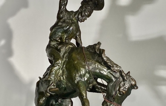 Alt text: Bronze sculpture of a cowboy riding on a bucking bronco, side view