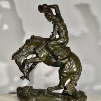 Alt text: Bronze sculpture of a cowboy riding on a bucking bronco, side view