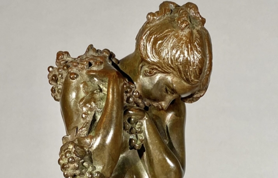 Alt text: Bronze sculpture of a nude woman standing and cradling grapes over her shoulder and into her chest, angle detail view