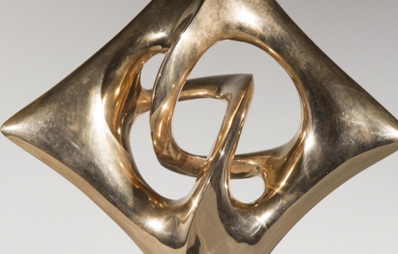 Alt text: Abstract diamond-shaped sculpture in bronze with points in each cardinal direction mounted on base, frontal view