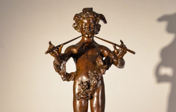 Bronze fountain sculpture of the deity Pan mischeviously playing two flutes, standing atop a sphere flanked by fish, frontal view