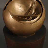 Alt text: Abstract bronze sphere atop a bronze column, angled view