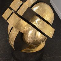 Alt text: Abstracted bronze sculpture that looks interlocking parts on a round base, close up view