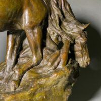 Alt text: Bronze sculpture of a horse bending down alongside a girl sitting near to the ground, peering over a cliff