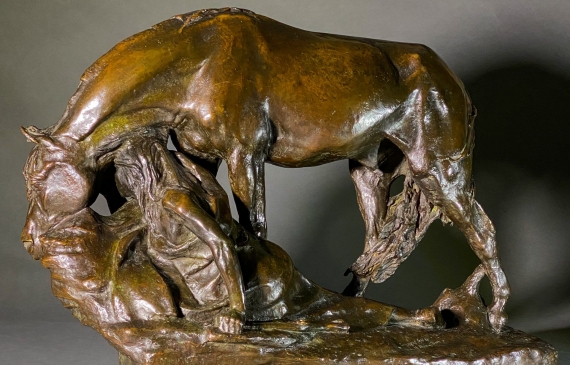 Alt text: Bronze sculpture of a horse bending down alongside a girl sitting near to the ground, peering over a cliff