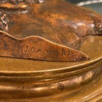 Alt text: Bronze relief sculpture of a man's head, signature detail