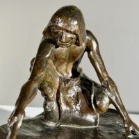 Alt text: Bronze sculpture of a crouching man with outstretched arm