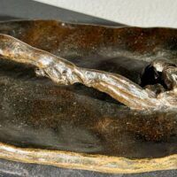 Alt text: Bronze sculpture, detail of a snake on a staff