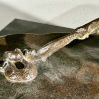 Alt text: Bronze sculpture, detail of a snake on a staff