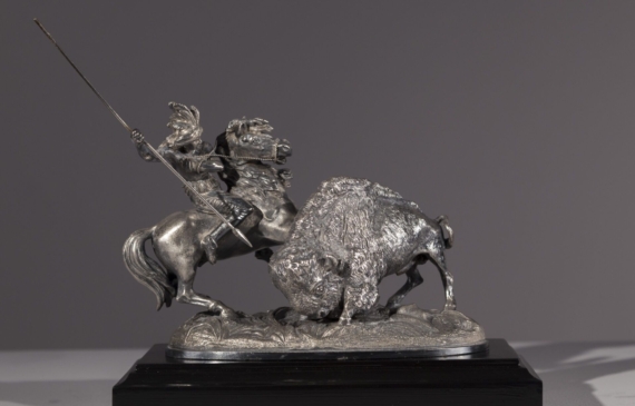 Alt text: Metal sculpture of a Native American man on horseback spearing a buffalo