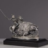 Alt text: Metal sculpture of a Native American man on horseback spearing a buffalo
