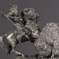 Alt text: Metal sculpture of a Native American man on horseback spearing a buffalo