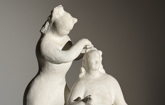 Alt text: Stylized, white sculpture of two women, one standing and one seated