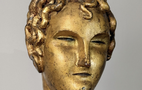 Alt text: Stylized, gilt bronze sculpture of a head of a boy with curly hair