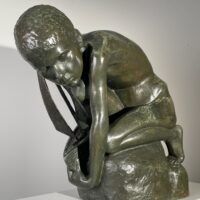 Alt text: Bronze sculpture of a crouching boy holding a sailboat