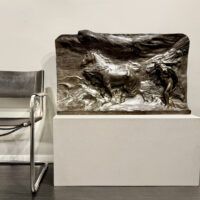 Alt text: Bronze relief of men with horses, next to a chair